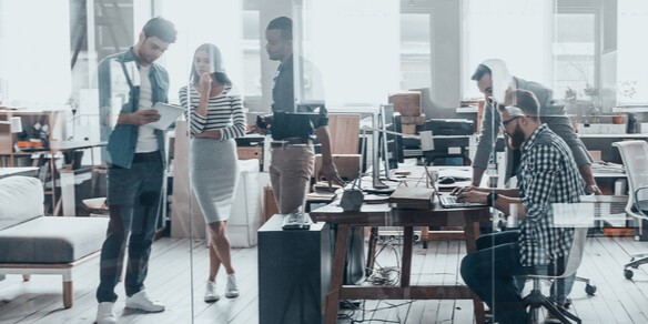 Mehrere Personen in einem Büro, die mit unterschiedlichen Geräten zusammenarbeiten
